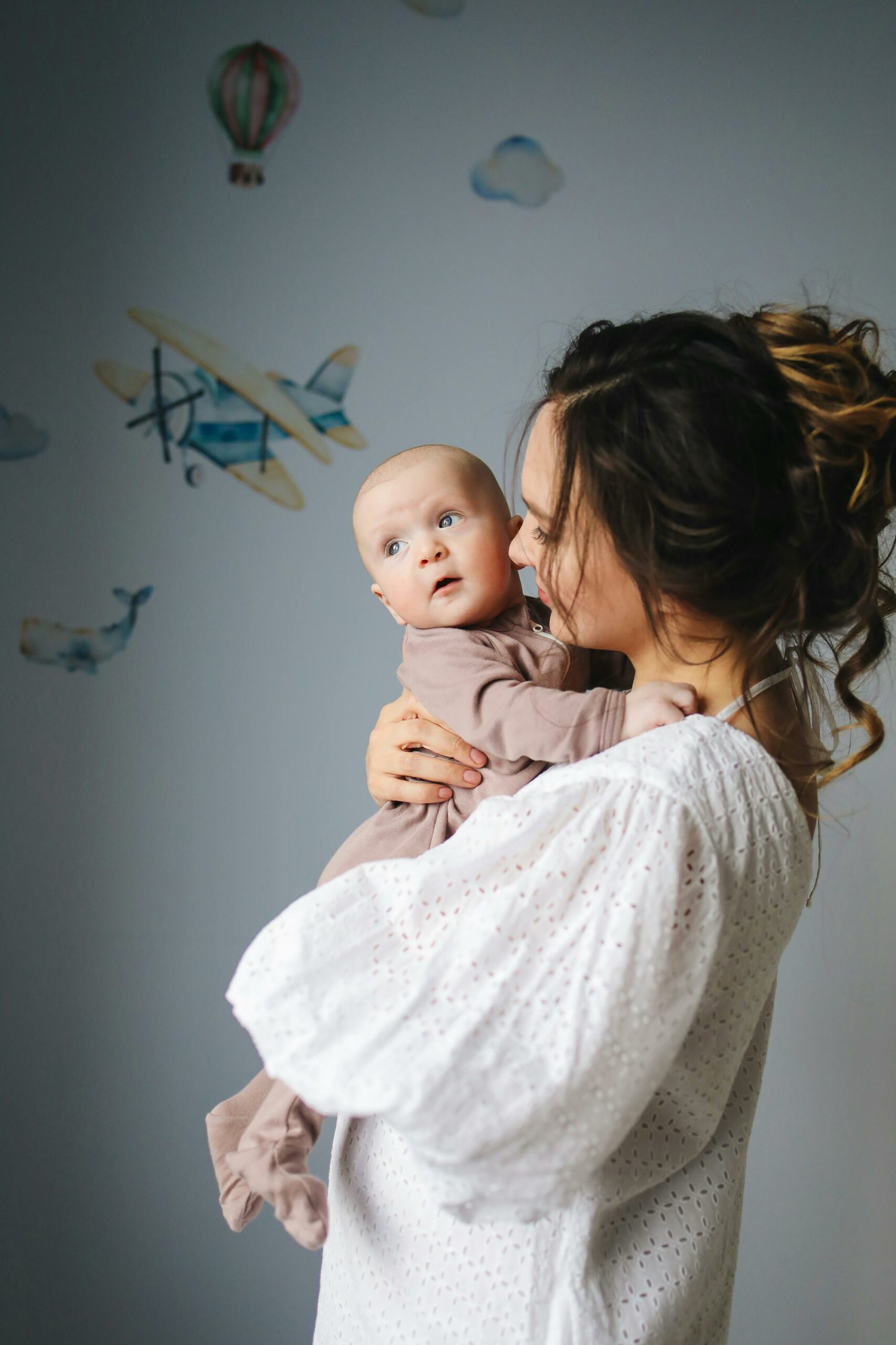 A mother lovingly holds her baby in a nursery decorated with airplanes.